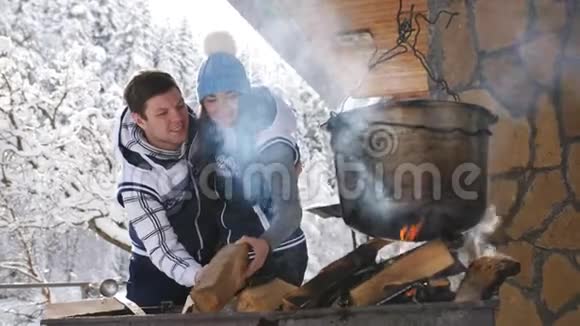 年轻的幸福夫妇在冬天的森林木屋里的院子里的烤架上做饭视频的预览图