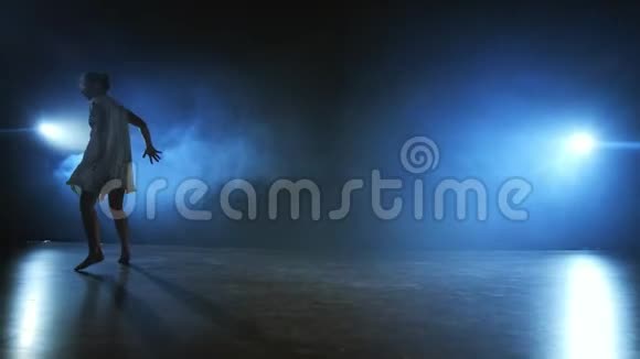 一个穿着白色连衣裙的女孩在舞台上和聚光灯下的烟雾一起跳舞视频的预览图