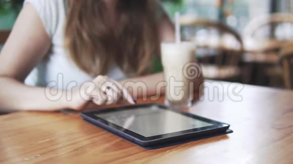年轻美丽的欧洲女孩在炎热的夏日在咖啡馆里使用平板电脑提供冷牛奶和咖啡鸡尾酒关门视频的预览图