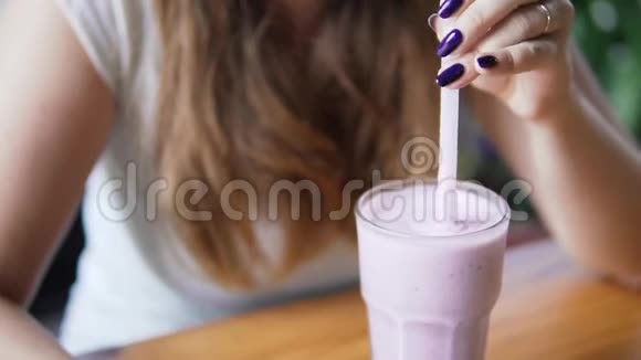 年轻美丽的欧洲女孩混合和喝冷牛奶鸡尾酒与蓝莓在咖啡馆在炎热的夏天妇女视频的预览图