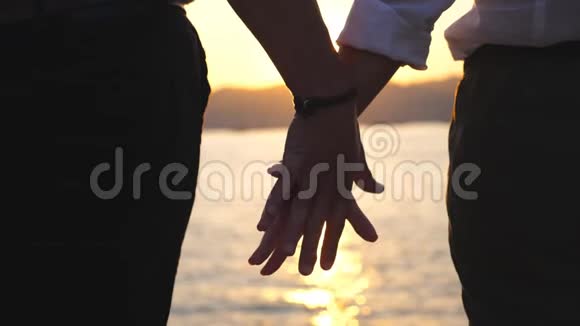 日落时分在海的背景下雌雄双手相握的剪影一对年轻夫妇视频的预览图