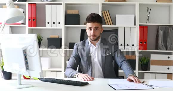 穿着灰色夹克的商人坐在白色办公室的桌子上消极地摇头视频的预览图