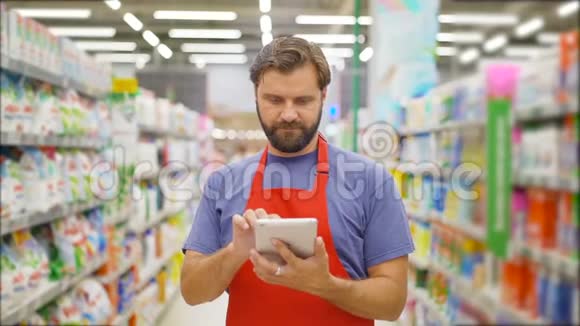 一位英俊的推销员用数字平板电脑站在超市的货架上视频的预览图