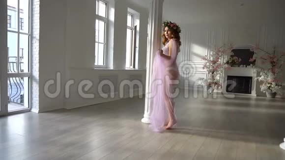 年轻的孕妇穿着淡蓝色的粉红色裙子在家跳舞视频的预览图