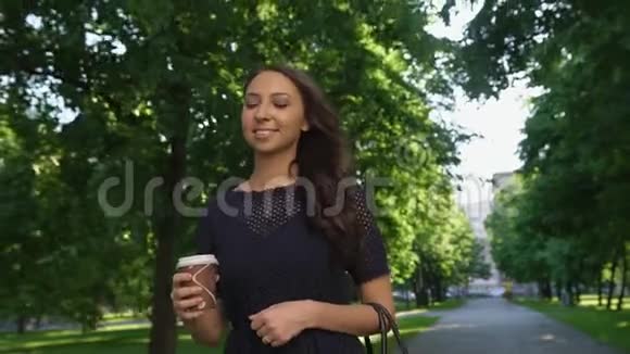 年轻美丽的黑发女孩带着咖啡走在夏天的公园里微笑着视频的预览图