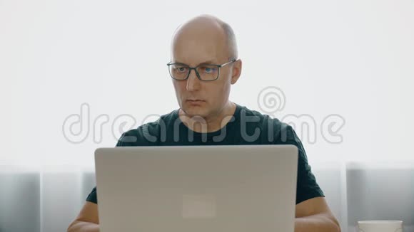 一个戴眼镜的男人的肖像在笔记本电脑后面工作开心地笑着这个人表现出快乐一个穿灰色T恤的快乐男人视频的预览图