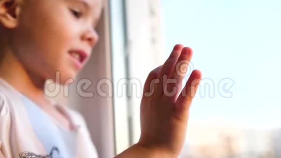 一个孩子站在窗户附近看着雪落在街上玻璃窗上的特写视频的预览图