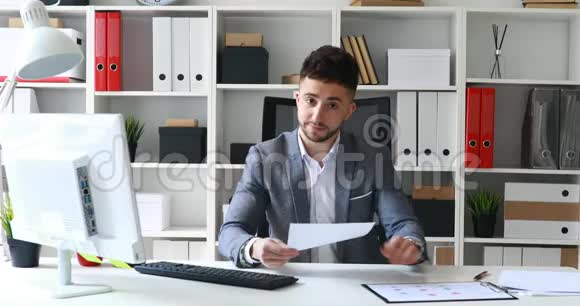 穿着灰色夹克的商人坐在白色办公室的桌子上提供文件视频的预览图