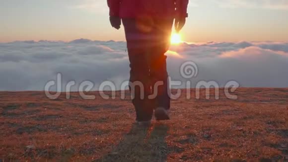 日出时穿着夹克和裤子的年轻女子正走在云层上方的高原边缘视频的预览图