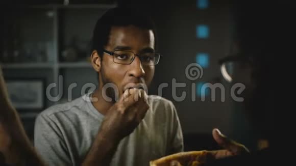 非洲裔美国休闲年轻人戴眼镜在聚会上吃披萨快乐的朋友在家里的厨房里享用快餐视频的预览图