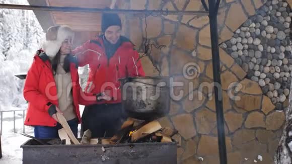 年轻的幸福夫妇在冬天的森林木屋里的院子里的烤架上做饭视频的预览图