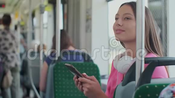 年轻时尚的女性使用公共交通工具坐在现代电车上带着电话和耳机视频的预览图