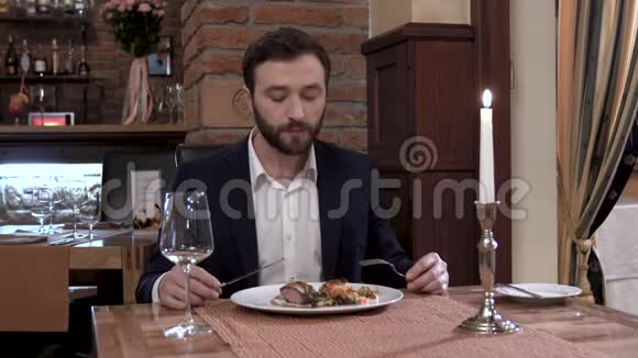 一个留着胡子的人坐在餐厅的桌子旁吃肉菜享受美食视频的预览图