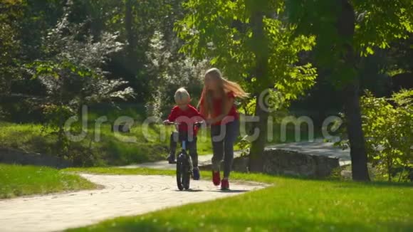 一个年轻女子慢镜头教她的小儿子骑自行车视频的预览图