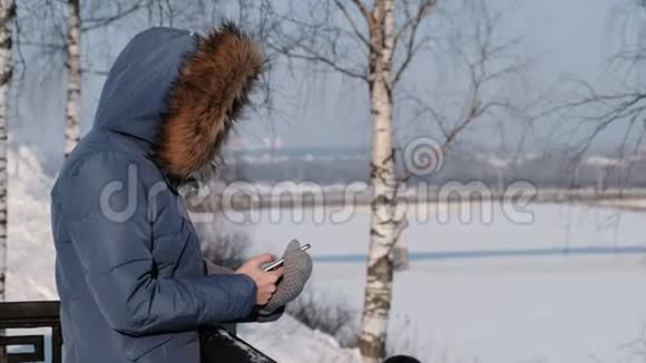 穿着蓝羽绒服的女人在冬天公园的手机里写短信侧视图视频的预览图