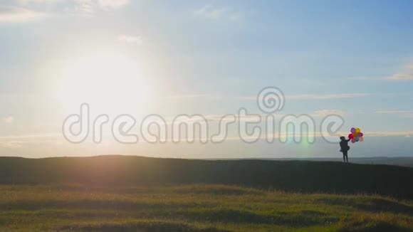日落时分坐着气球在田野里散步的剪影女孩日落时带着气球在田野里快乐的孩子视频的预览图