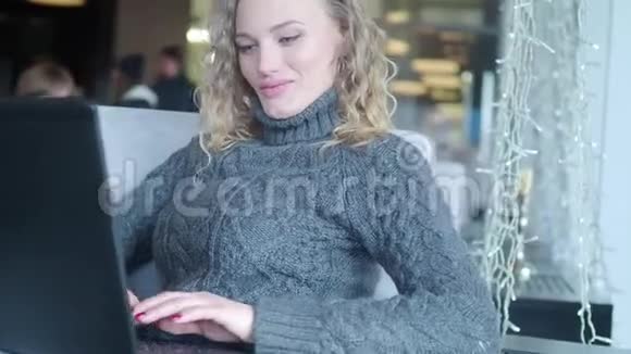 漂亮的时髦女人在咖啡馆里用笔记本电脑她发短信微笑着视频的预览图