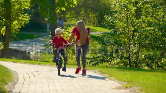 一个年轻女子慢镜头教她的小儿子骑自行车视频的预览图