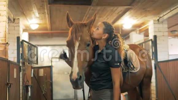 一个女人和一匹棕色的马在一个马厩里靠近视频的预览图