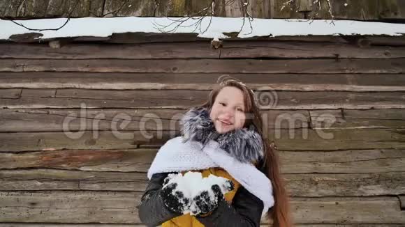 年轻漂亮的女孩在镜头前尽情地吹雪穿着冬天的衣服在木屋的背景下视频的预览图