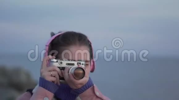 戴着耳机的女孩在她的老式相机上拍下了大海日落的照片视频的预览图
