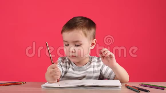 可爱的小男孩用铅笔在粉红色背景的相册里画画视频的预览图