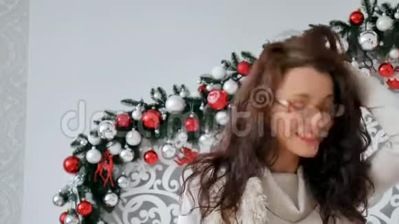 圣诞装饰背景下一个穿着眼镜和温暖毛衣的快乐黑发女孩的肖像可爱的女孩视频的预览图