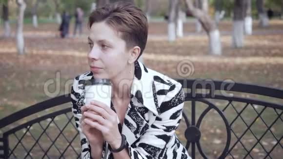 女人坐在公园的长凳上放松和喝咖啡视频的预览图