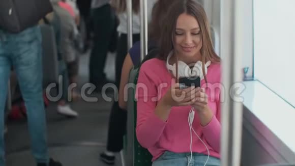 年轻时尚的女性使用公共交通工具坐在现代电车上带着电话和耳机视频的预览图