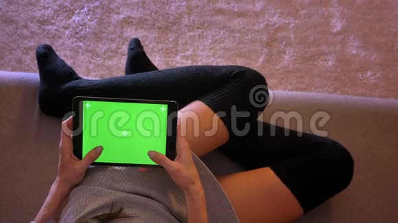 绿色屏幕的平板电脑上的温柔性感女性短信特写肖像女孩腿在舒适的位置视频的预览图