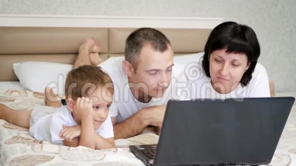 幸福家庭爸爸妈妈和儿子躺在床上看着笔记本电脑屏幕视频的预览图
