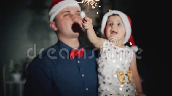 快乐的一家人头戴圣诞老人帽戴着闪闪发光的首饰在圣诞树下微笑视频的预览图