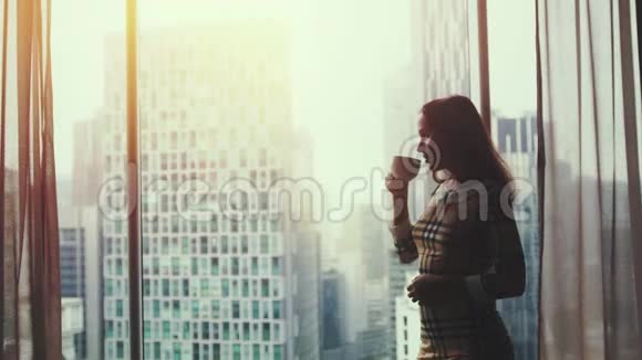 年轻漂亮的女人在日落时喝着咖啡从窗外欣赏风景3840x2160视频的预览图