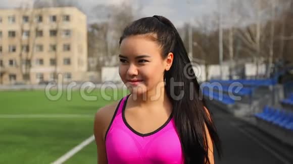 亚洲年轻的运动女孩手里拿着一瓶水训练后正在体育场散步视频的预览图