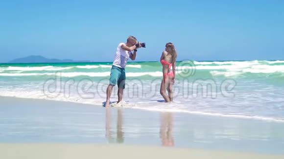 男子摄影师拍摄年轻女子比基尼在海边摆姿势年轻的摄影师视频的预览图