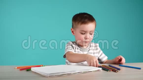 可爱的小男孩用铅笔在蓝色背景的相册里画画视频的预览图