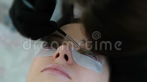 美容治疗美容师用刷子在卷发器睫毛上涂上一种溶液睫毛层压板特写的脸视频的预览图