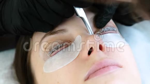 美容治疗美容师用镊子从睫毛上取出溶液睫毛层压板特写的脸视频的预览图