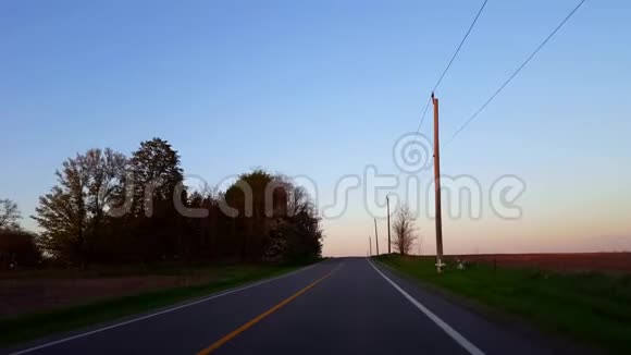 日落时驾驶农村公路太阳在黄昏时在地平线上升起时的驱动视角视频的预览图