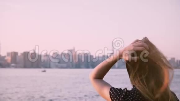 快乐的年轻白种人女孩戴着太阳镜头发随风飘动在城市河滩观看日落慢动作视频的预览图