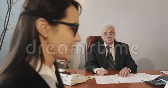 一位头发花白的老商人邀请黑发女人到他的办公室开会视频的预览图