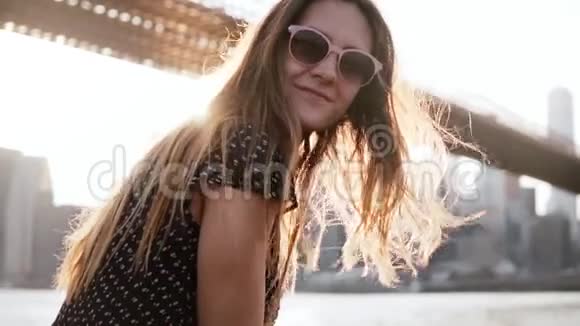 慢动作快乐的女孩戴着太阳镜带着令人惊叹的金色头发在布鲁克林大桥的镜头前微笑视频的预览图