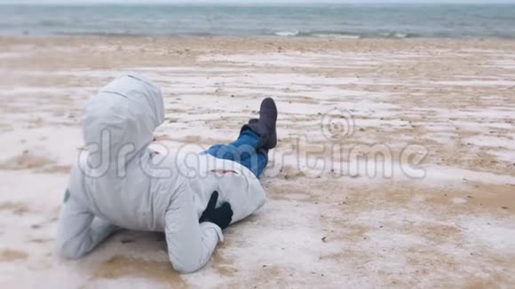 冬天女游客躺在海边一片雪白的沙滩上穿夹克和牛仔裤的女人后视图视频的预览图