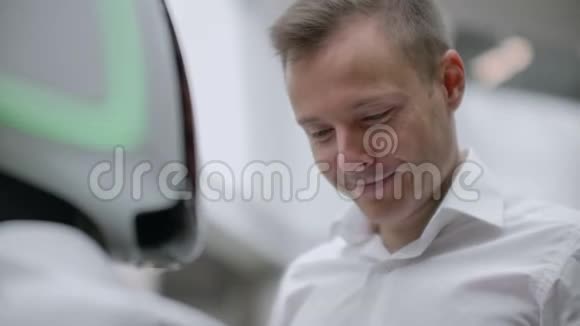 一个穿衬衫的男人和一个白色机器人交流他问问题用手指按屏幕视频的预览图