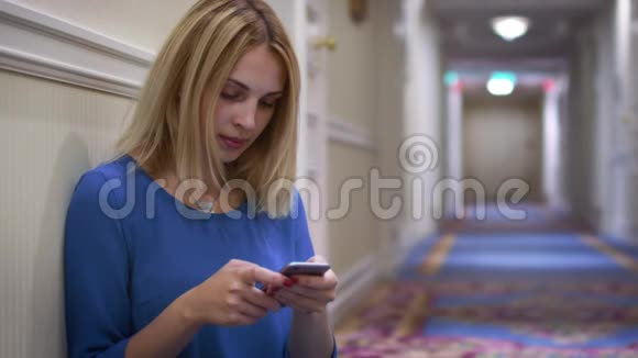 坐在地板上的女人靠在长长的走廊上的墙上用手机视频的预览图