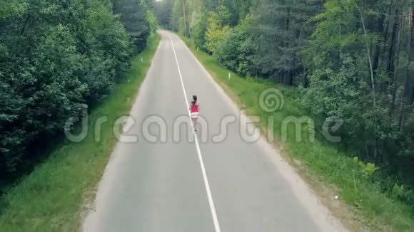 鸟瞰一条森林道路和一个苗条的年轻女子穿过它视频的预览图