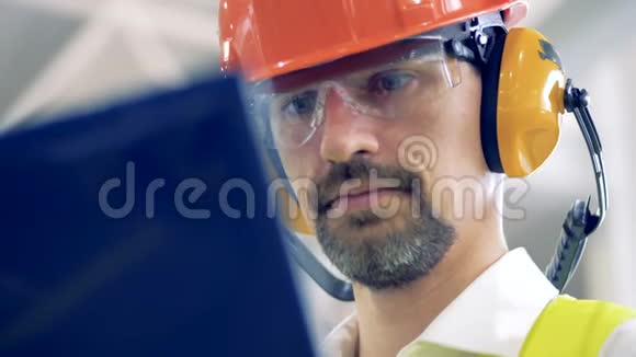 一个戴着安全帽的人在仓库的笔记本电脑上工作关门视频的预览图