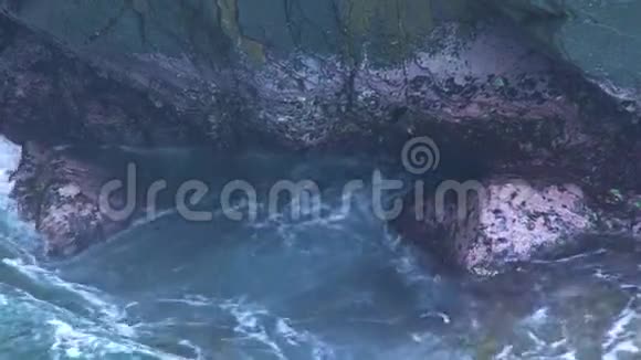 蓝色的海浪溅在岩石岛上波浪与泡沫破裂的岩石悬崖透明的海水和大石头视频的预览图