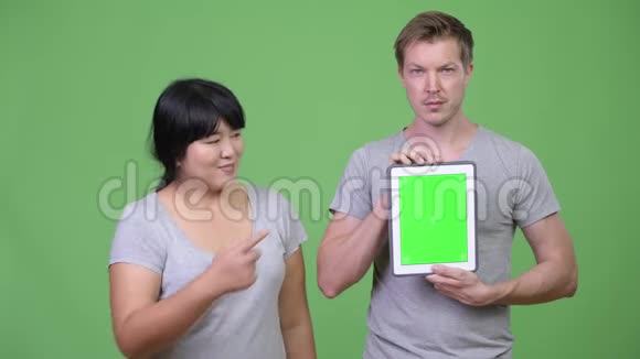 年轻快乐的多民族夫妇一起展示数字平板电脑并竖起大拇指视频的预览图