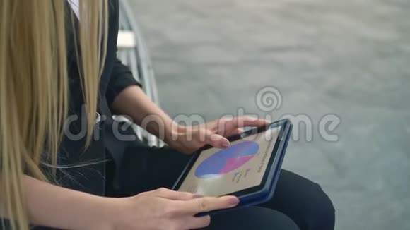 女人在长凳上用平板电脑正式的女商人坐在办公室露台的长凳上休闲地浏览平板电脑视频的预览图
